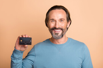 Photo portrait of middle-aged man showing credit debit card smiling isolated on pastel beige color background