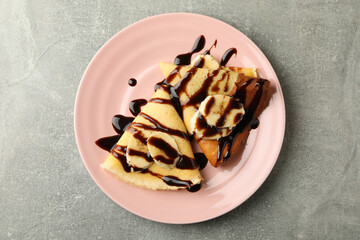 Plate of crepes with chocolate sauce and banana slices on gray background