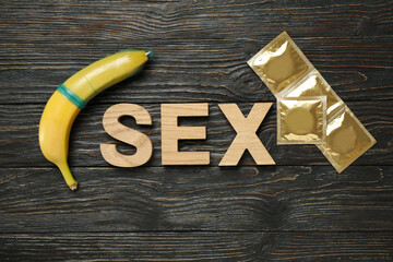 Word Sex, banana and condoms on wooden background