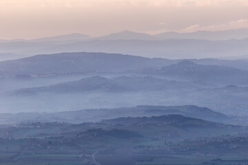Mist and fog between valley and layers of mountains and hills at dusk, in Umbria (Italy)