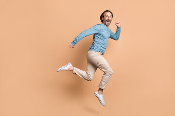 Fototapeta na wymiar Full length photo portrait of happy man running jumping up isolated on pastel beige colored background
