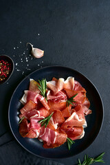 Slices of prosciutto di parma or jamon serrano (iberico)  on a black plate. Top view with copy...