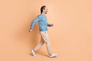 Fototapeta na wymiar Full length profile photo of guy walk wear eyewear blue pullover pants sneakers isolated beige color background