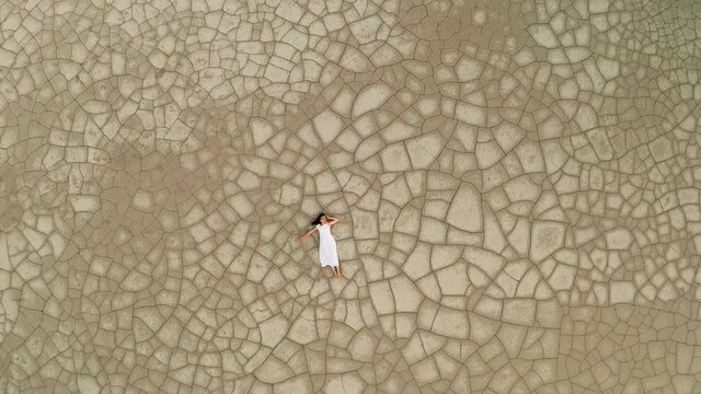 Aerial view of a woman lying on the cracked ground. Environmental protection concept, global warming