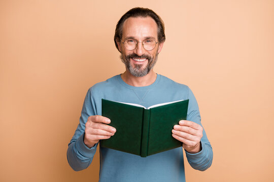 Photo portrait of man holding green book reading isolated on pastel beige colored background