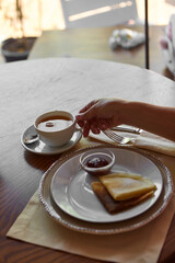 Cropped shot of person drinking tea and eating pancakes at wooden table