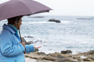 senior woman with coat and umbrella in front of the coast