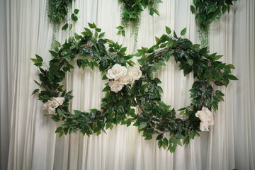 Green leaves and white flowers wreath hanging on white curtains 