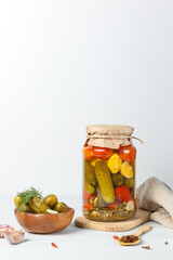 Fermented vegetables in a glass jar. Pickled cucumbers, tomatoes and squash, vertically on a light background