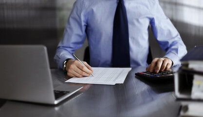 Unknown man accountant in blue shirt use calculator and computer with holding pen on while staying at home during covid pandemic. Taxes and audit concept