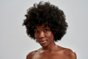 Beauty portrait of attractive african american young woman with afro hair and perfect smooth glowing skin looking at camera while posing isolated over gray background