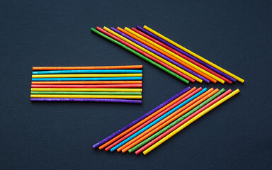 Arrow sign made of colorful wooden sticks isolated on black background; multicolored arrow; top view, flat lay