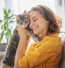 Close-up portrait of a beautiful cheerful young woman with a cute gray cat in her arms at home