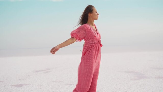 Freedom woman in blowing airness pink dress and hat standing on salty beach on pink lake. Paradise resort getaway destination at idyllic landscape in Ukraine
