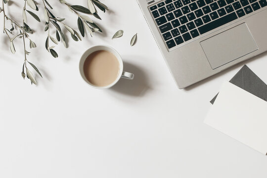 Summer workspace composition. Blank greeting card mock-up scene. Cup of coffee, olive tree branches and laptop isolated on white table background. Flat lay, top view. Blogger design. Home office.