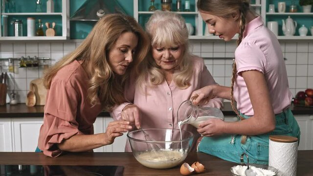 Cinematic footage of a three generations family preparing a cake in the kitchen. Grandmother, mother, and daughter having fun togheter at home