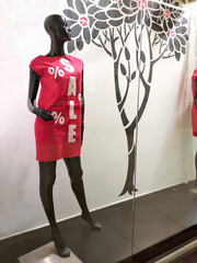 A black mannequin in a red dress with the inscription Sale on the window of the clothing store. Discounts and promotions in the store