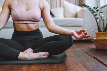 Anonymous young woman sit in lotus yoga position at home in living room. Relaxing state of mind, meditation.