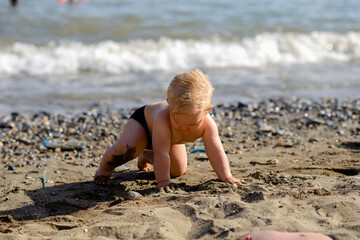  little lovely baby playing with stones and sand at the seaside. Attractive child having fun, enjoying holidays at sea together.