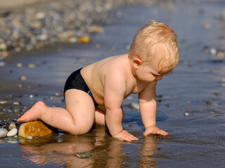  little lovely baby playing with stones and sand at the seaside. Attractive child having fun, enjoying holidays at sea together.