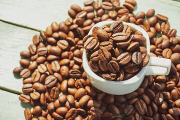 Roasted coffee beans and white cup on the wooden background.