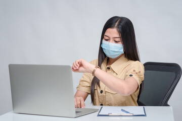 A young Asian woman wearing a COVID-19 mask and she is looking at the watch on her wrist. To see when to stop working