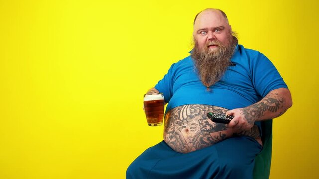 Funny man watching television. Big fat hipster with tattoo on yellow colored background