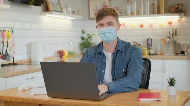 quarantine, remote job and pandemic concept - middle-aged man wearing face protective medical mask for protection from virus disease with laptop computer working at home