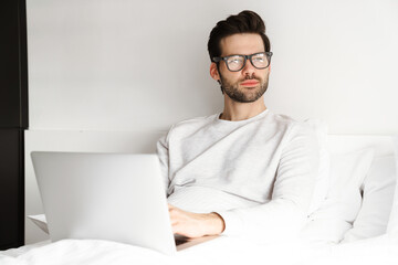 Focused handsome man using laptop while resting in bed