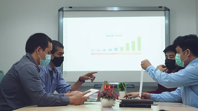 Businessmen wearing protective masks discussing and work together in meeting room. Social distance practice prevent coronavirus COVID-19.