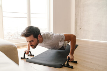 Focused athletic man doing exercise with push-up stops while working out