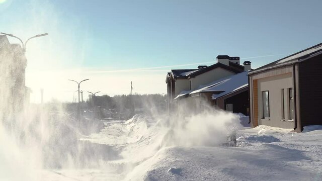 A man with a snowblower removes snow from the street near his house.