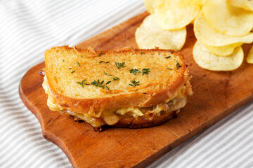 Homemade French Onion Melt Cheese Sandwich with Chips on a rustic wooden board on cloth, low angle view.