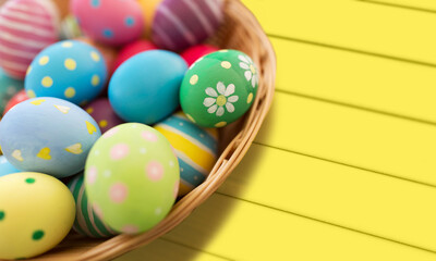 Fototapeta na wymiar easter, holidays and tradition concept - close up of colored eggs in basket over yellow wooden boards background