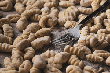 floured fork holding a gnocchi, background with many gnocchi, homemade food
