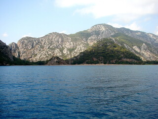 Panorama of the blue sea surface on the background of mountain ranges illuminated by the morning sun on the horizon.