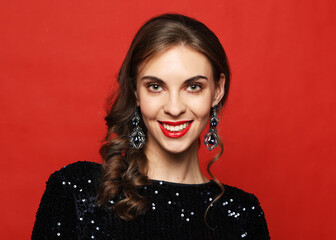 Amazing luxury woman in stylish party dress posing on red background . Close up portrait. Bright smokey eyes make up, red full lips, healthy wavy hairs.