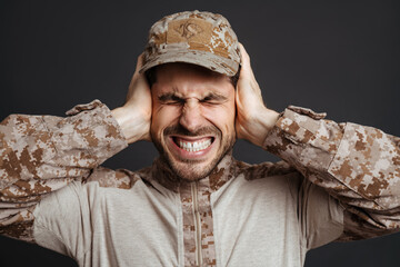 Unhappy masculine military man grimacing while covering his ears