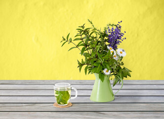 eco and organic concept - herbal tea and flowers in green rustic jug on wooden table over yellow background
