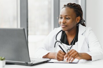 medicine, online service and healthcare concept - happy smiling african american female doctor or nurse with headset and laptop having conference or video call at hospital