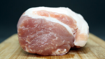 A piece of pork on a wooden board on a black background.