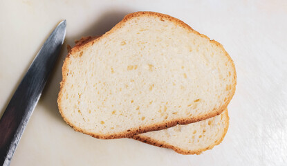 Two cut pieces of a white loaf on a light surface with a knife lying next to it.