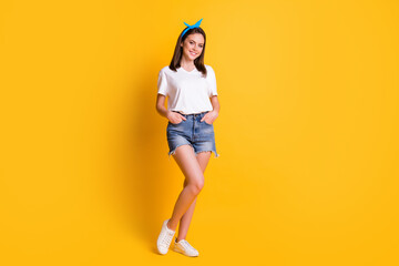 Fototapeta na wymiar Full body photo of attractive young woman hold hands in pockets beaming smile isolated on yellow color background
