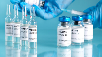 Coronavirus vaccination with vaccine bottles and ampoules. Doctor's hand holds syringe and vaccine vial for coronavirus cure. Covid-19 vaccine in researcher hands. Clinical trial during pandemic.