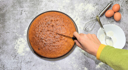 Homemade sponge cake, part of the ingredients and utensils. Cutting a portion. On a stone base and zenith view.