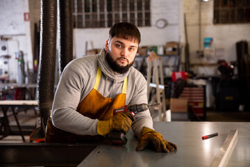 Fototapeta na wymiar Portrait of confident man mechanic drilling metal sheet in workshop