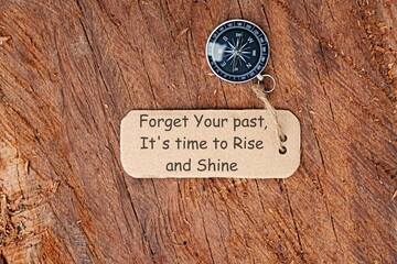 Conceptual Image: Magnetic compass with paper tag written Forget Your Past, It's Time To Rise And Shine, selective focus.