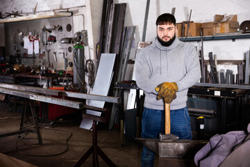 Fototapeta na wymiar Young man mechanic working with hand hammer in workshop