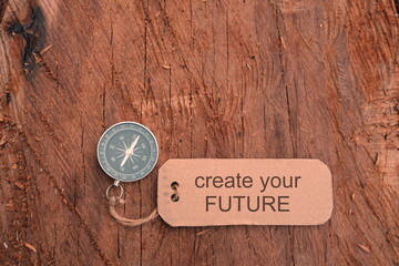 Conceptual Image: Magnetic compass with paper tag written Create Your Future at outdoor, selective focus.