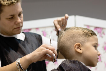 Below view of hairdresser cutting boy's hair at the salon.